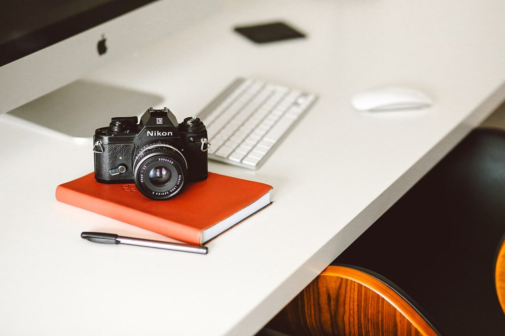 Fotoğraf makinesi ve defter ile bilgisayar masası