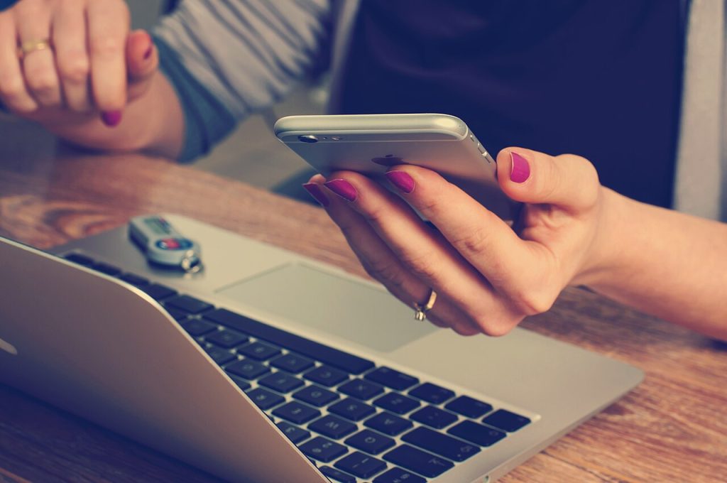 Bilgisayar yanında telefondan bilgi inceleyen kişiler